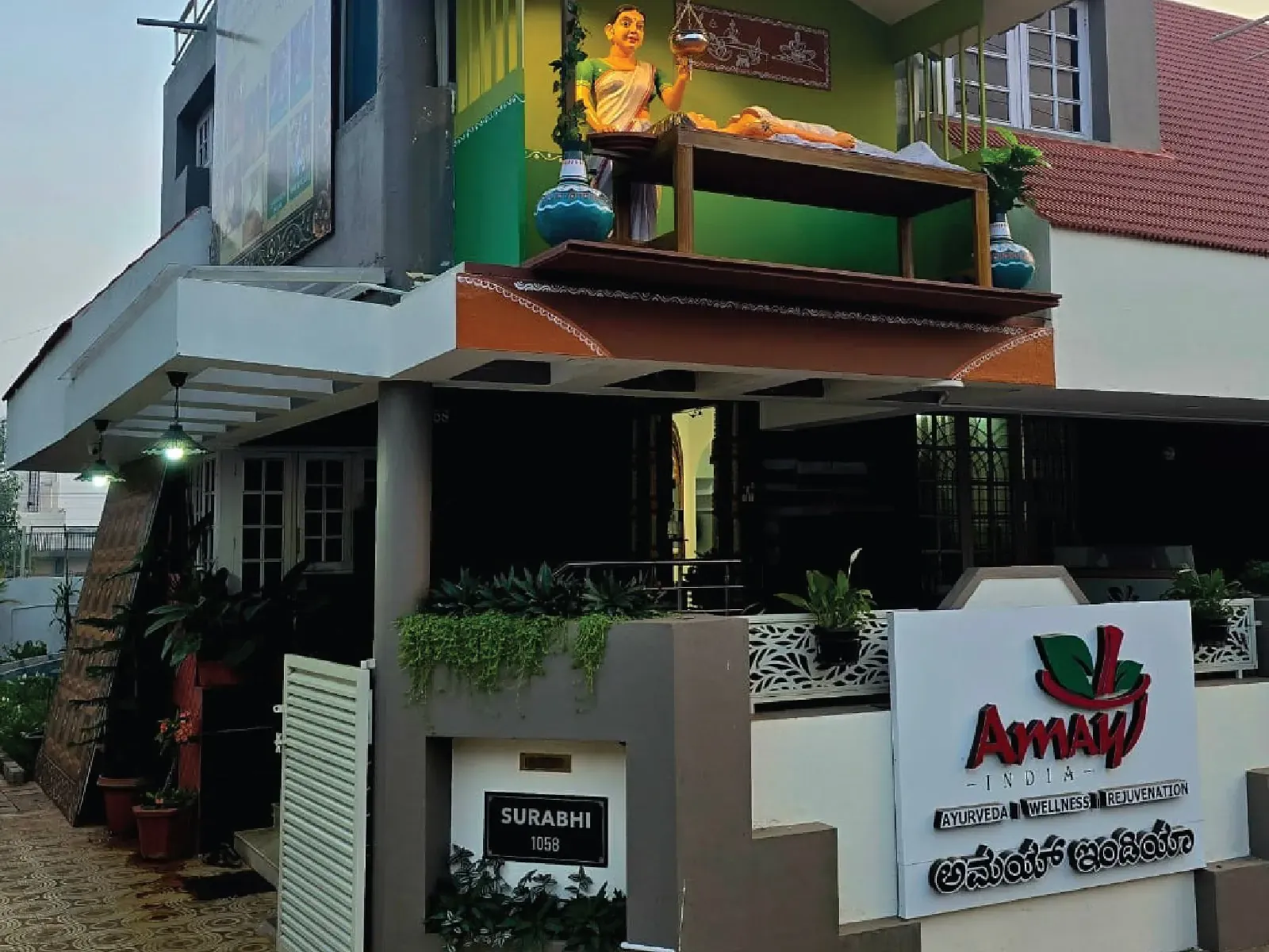 Entrance of the Surabhi 1058 building with the Amay India signboard and a Shirodhara sculpture on the balcony